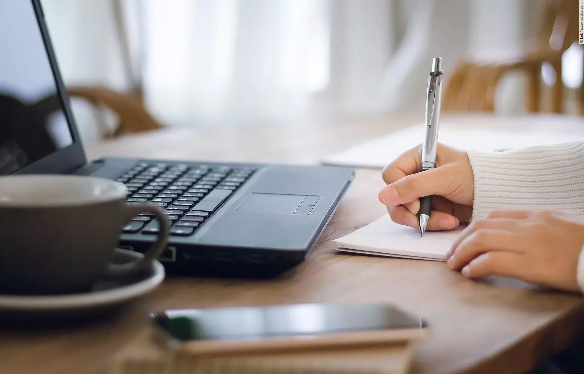 Close-up. girl hand writing on paperwork while she working with laptop on desk Nahaufnahme von einer am Schreibtisch arbeitenden Person.