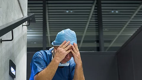 Tensed male surgeon sitting with hands on forehead on staircase