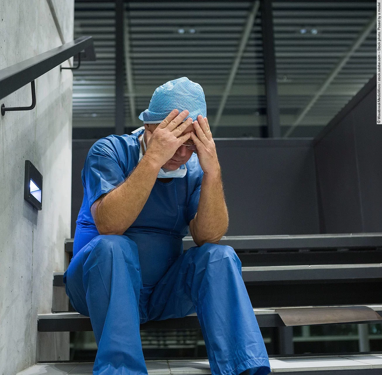 Tensed male surgeon sitting with hands on forehead on staircase