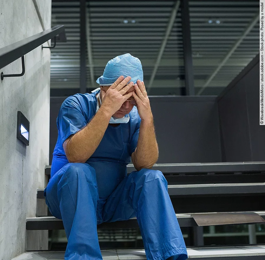 Tensed male surgeon sitting with hands on forehead on staircase