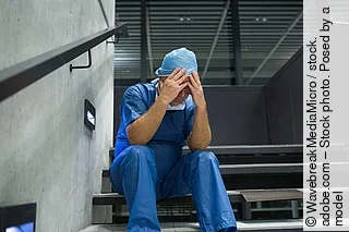 Tensed male surgeon sitting with hands on forehead on staircase