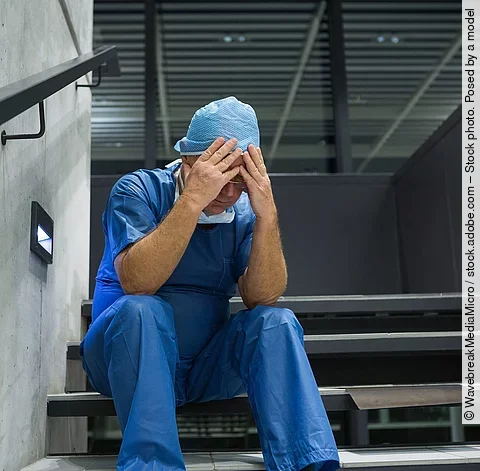 Tensed male surgeon sitting with hands on forehead on staircase