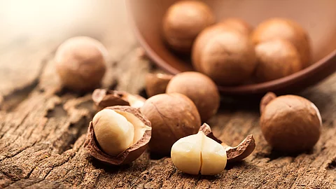 Mehrere Macadamianüsse liegen in einer Holzschale auf einem hölzernen Tisch.