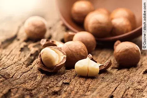 Mehrere Macadamianüsse liegen in einer Holzschale auf einem hölzernen Tisch.