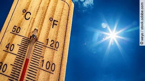 Nahaufnahme von einem Thermometer, das 40 Grad Celsius anzeigt. Im Hintergrund ist ein strahlen blauer Himmel mit nur sehr kleinen und wenig Wolken. Die Sonne strahlt stark. 