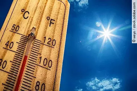 Nahaufnahme von einem Thermometer, das 40 Grad Celsius anzeigt. Im Hintergrund ist ein strahlen blauer Himmel mit nur sehr kleinen und wenig Wolken. Die Sonne strahlt stark.