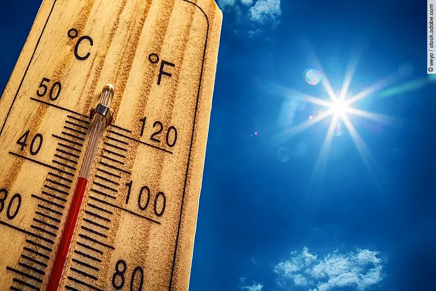 Nahaufnahme von einem Thermometer, das 40 Grad Celsius anzeigt. Im Hintergrund ist ein strahlen blauer Himmel mit nur sehr kleinen und wenig Wolken. Die Sonne strahlt stark.