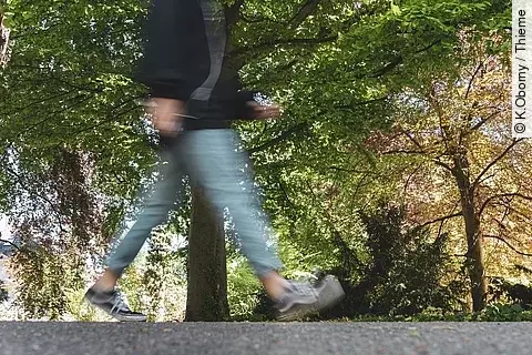 Eine durch die Fotografie verschwommene Person geht durch einen Park spazieren.