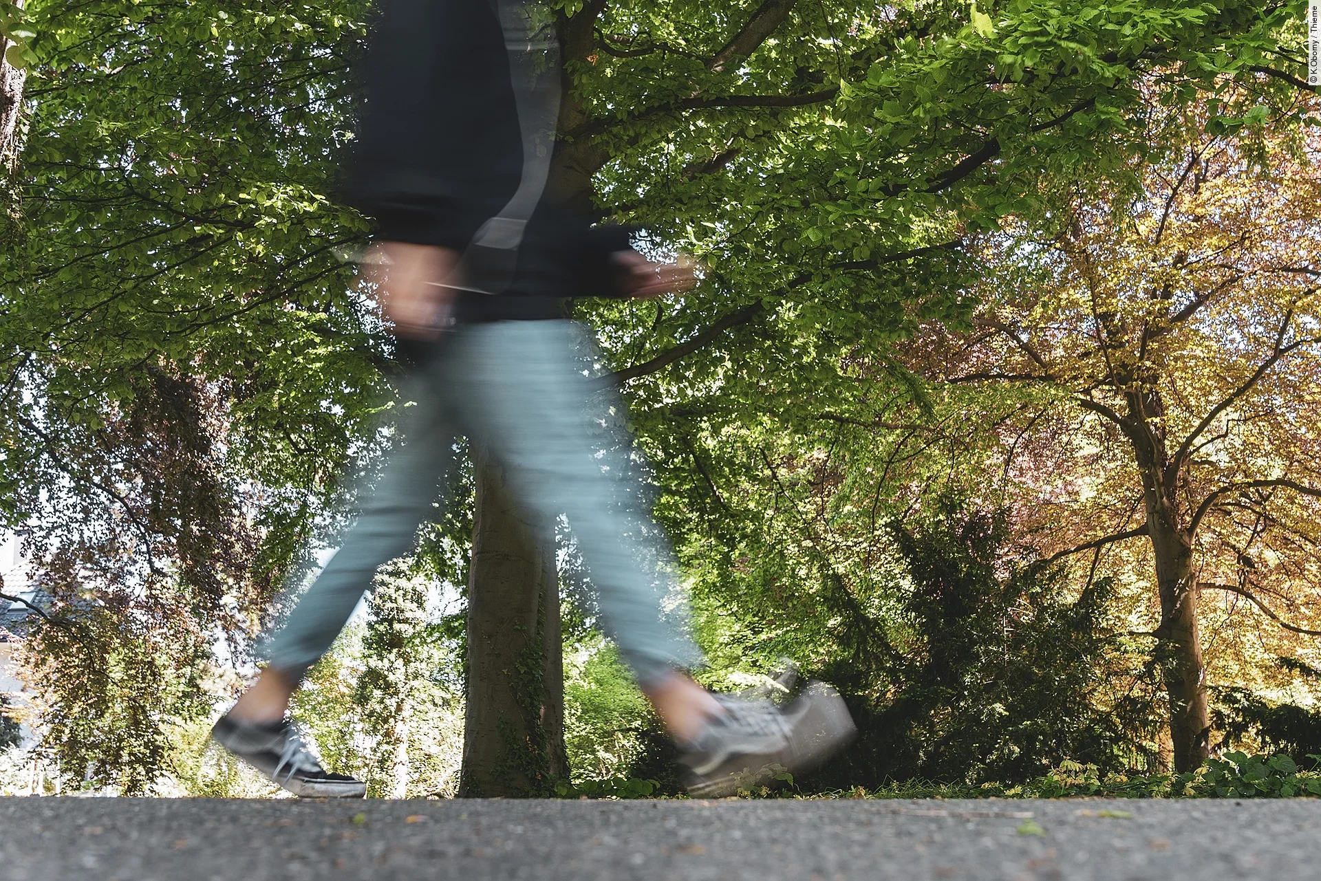 Eine durch die Fotografie verschwommene Person geht durch einen Park spazieren.