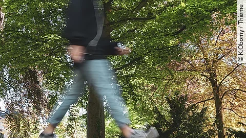 Eine durch die Fotografie verschwommene Person geht durch einen Park spazieren. Eine durch die Fotografie verschwommene Person geht durch einen Park spazieren.