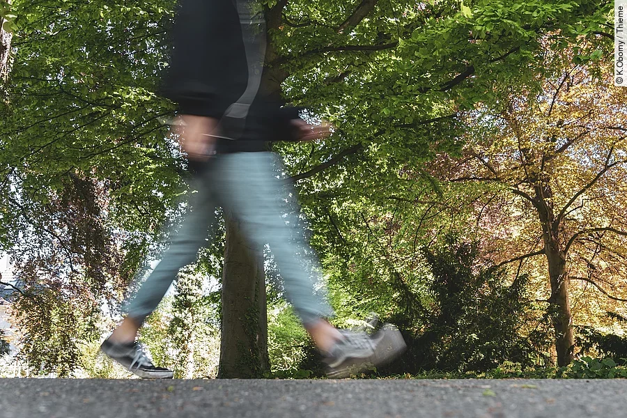 Eine durch die Fotografie verschwommene Person geht durch einen Park spazieren.
