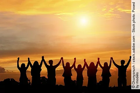 Im Sonnenuntergang stehen 8 Menschen, die sich an den Händen fassen und sie jubelnd hochgezogen haben.