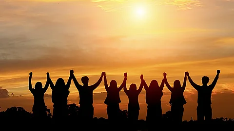 Im Sonnenuntergang stehen 8 Menschen, die sich an den Händen fassen und sie jubelnd hochgezogen haben.