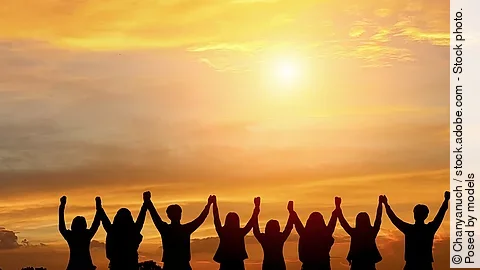 Im Sonnenuntergang stehen 8 Menschen, die sich an den Händen fassen und sie jubelnd hochgezogen haben.