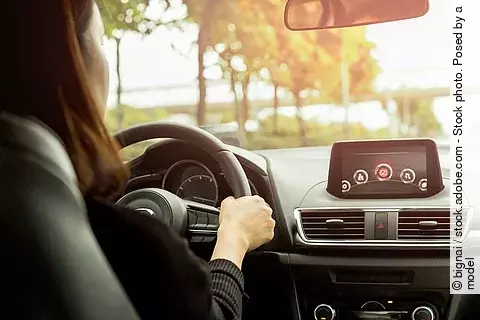 Eine Person steuert ein modernes Auto und fährt über eine Landstraße. 