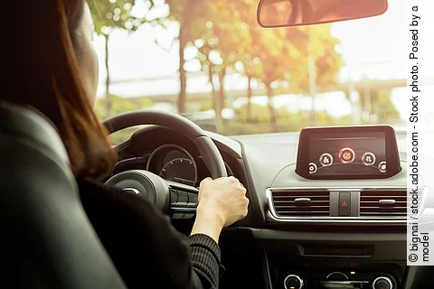 Eine Person steuert ein modernes Auto und fährt über eine Landstraße. 