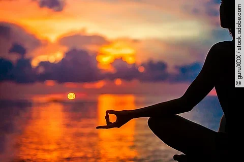 Eine Frau meditiert zur Entspannung am Meer im Sonnenuntergang.