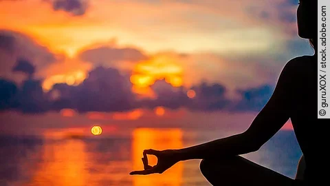 Eine Frau meditiert zur Entspannung am Meer im Sonnenuntergang.