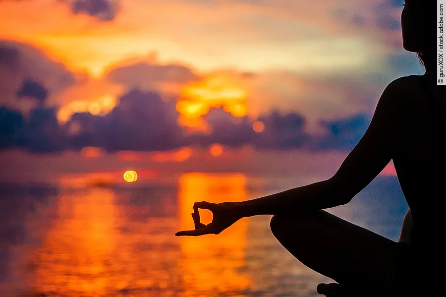 Eine Frau meditiert zur Entspannung am Meer im Sonnenuntergang.