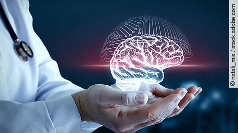 Hände von einer Person mit weißem Kittel halten ein virtuelles Gehirn fest