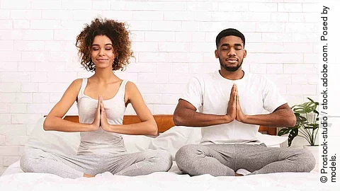 Peaceful african man and woman meditating in namaste position on bed