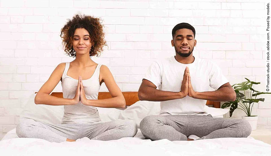 Peaceful african man and woman meditating in namaste position on bed