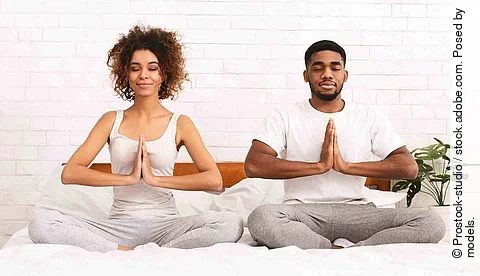 Peaceful african man and woman meditating in namaste position on bed