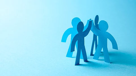 Eine Grafik zeigt blaue schemenhaft dargestellte Menschen, die im Kreis stehen und sich ein High Five geben.