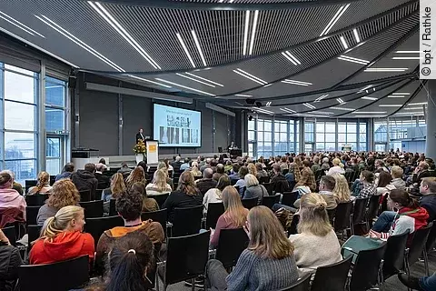 In einem Hörsaal sitzen viele Menschen und hören einem Vortrag an.