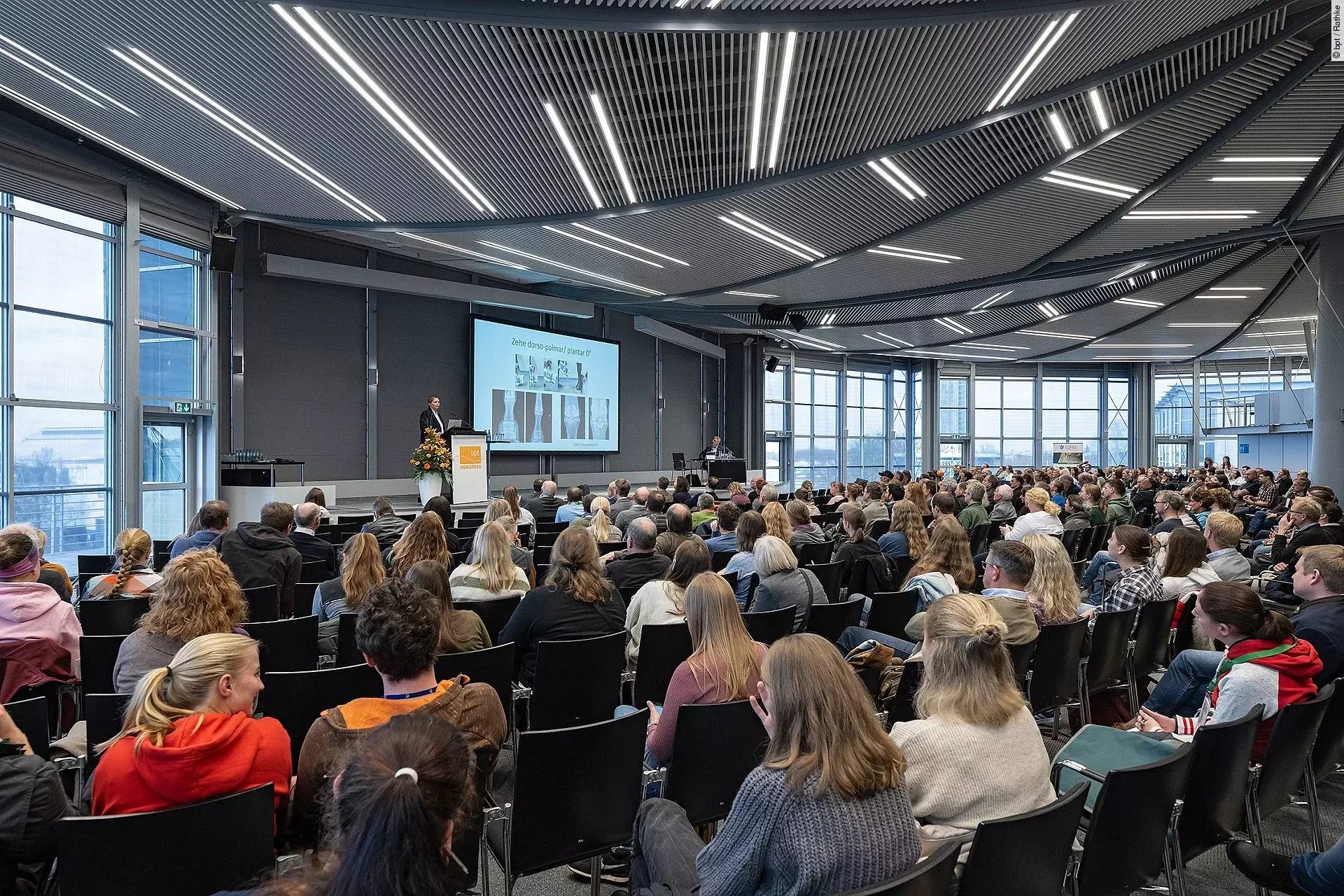 In einem Hörsaal sitzen viele Menschen und hören einem Vortrag an.