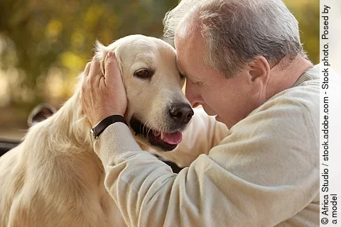 Ein Mann sitzt mit einem Hund und streichelt den Kopf des Hundes.