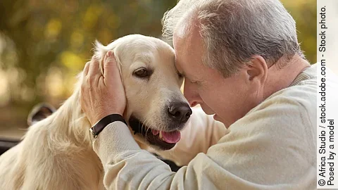 Ein Mann sitzt mit einem Hund und streichelt den Kopf des Hundes.
