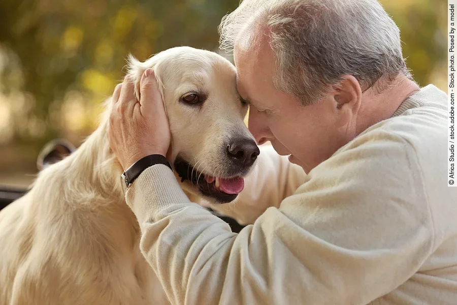 Ein Mann sitzt mit einem Hund und streichelt den Kopf des Hundes.