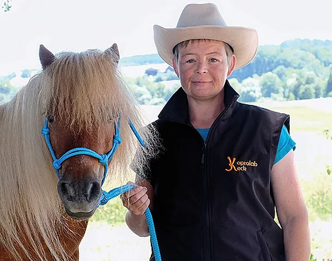 Nana Keck trägt einen beigen Cowboyhut und posiert mit einem braunen Pony für die Kamera.