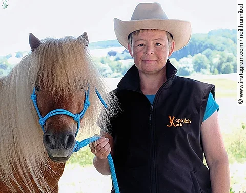 Nana Keck trägt einen beigen Cowboyhut und posiert mit einem braunen Pony für die Kamera.