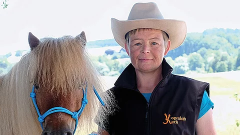 Nana Keck trägt einen beigen Cowboyhut und posiert mit einem braunen Pony für die Kamera.
