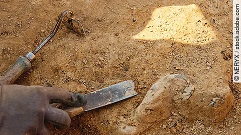 Ein*e Archäolog*in arbeitet mit Handwerkezeugen auf dem Boden. 