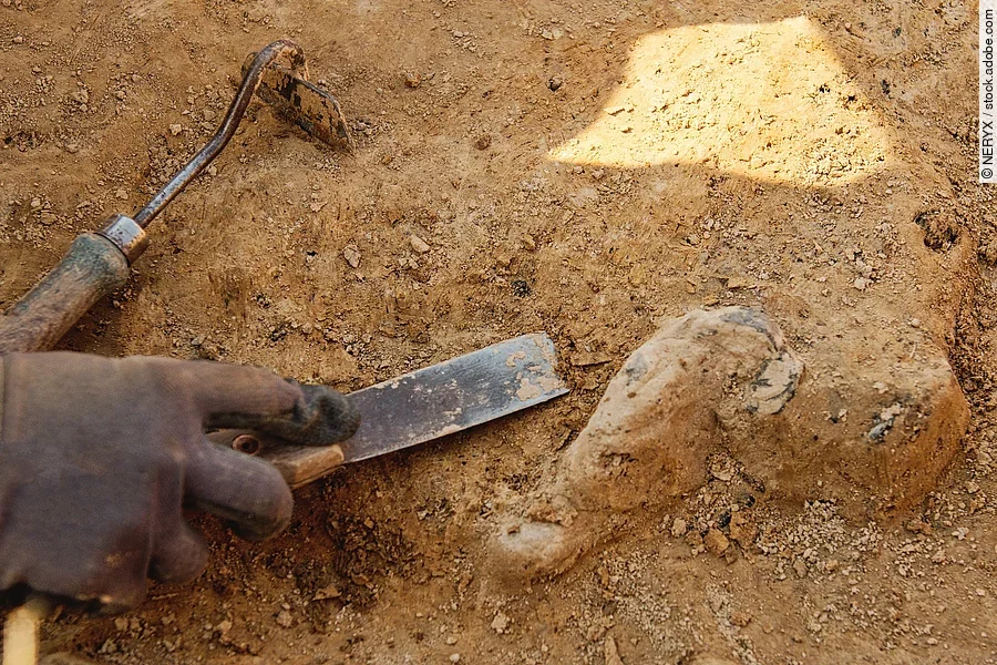 Ein*e Archäolog*in arbeitet mit Handwerkezeugen auf dem Boden. 
