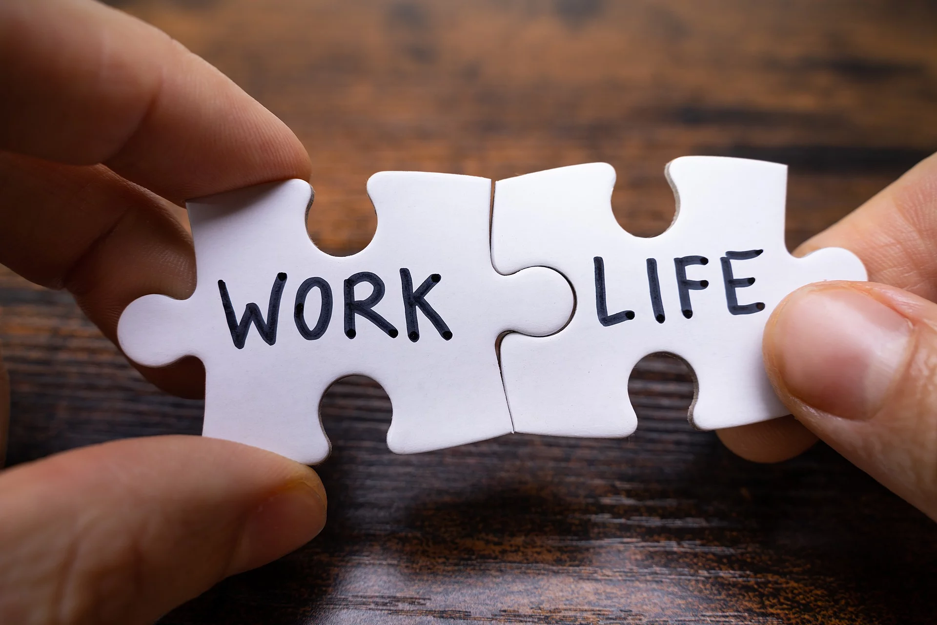 Zwei weiße Puzzleteile werden passend aneinander gehalten. Auf dem linken Teil steht in schwarzer Schrift "WORK" und auf dem anderen Puzzleteil steht "LIFE". 