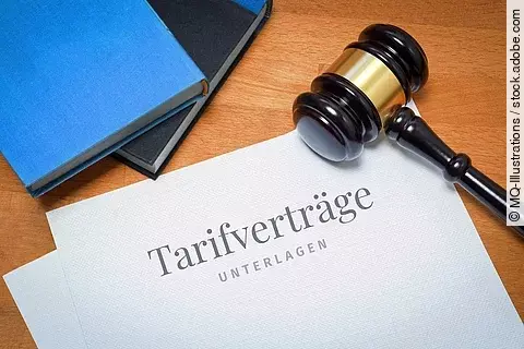Auf einem Holztisch liegt ein Dokument. Auf der Vorderseite des Dokuments steht "Tarifverträge Unterlagen". Rechts der Tarifverträge leit ein Richterhammer und oberhalb sind die Kanten von einem blauen und einem schwarzen Buch erkennbar. 