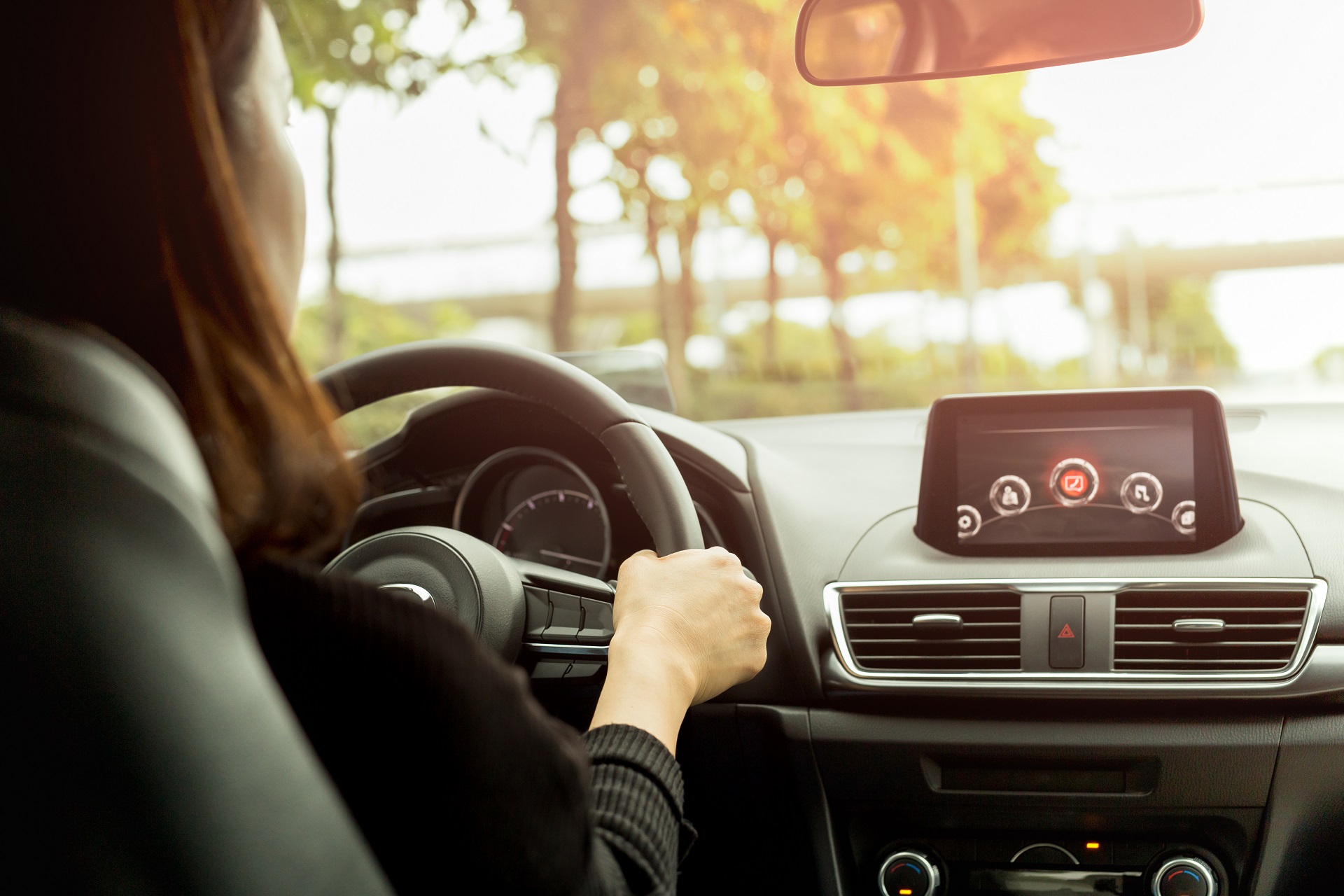 Woman driving her modern car on country road in sunlight. Eine Person steuert ein modernes Auto und fährt über eine Landstraße.