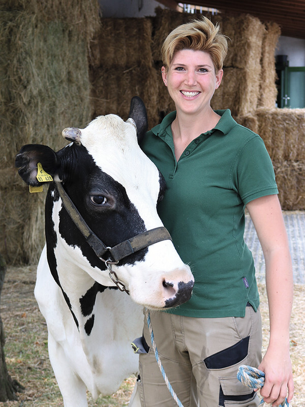 Juliane Bach trägt Arbeitskleidung und steht neben der Klinikskuh "Trudi" der Universität Gießen.
