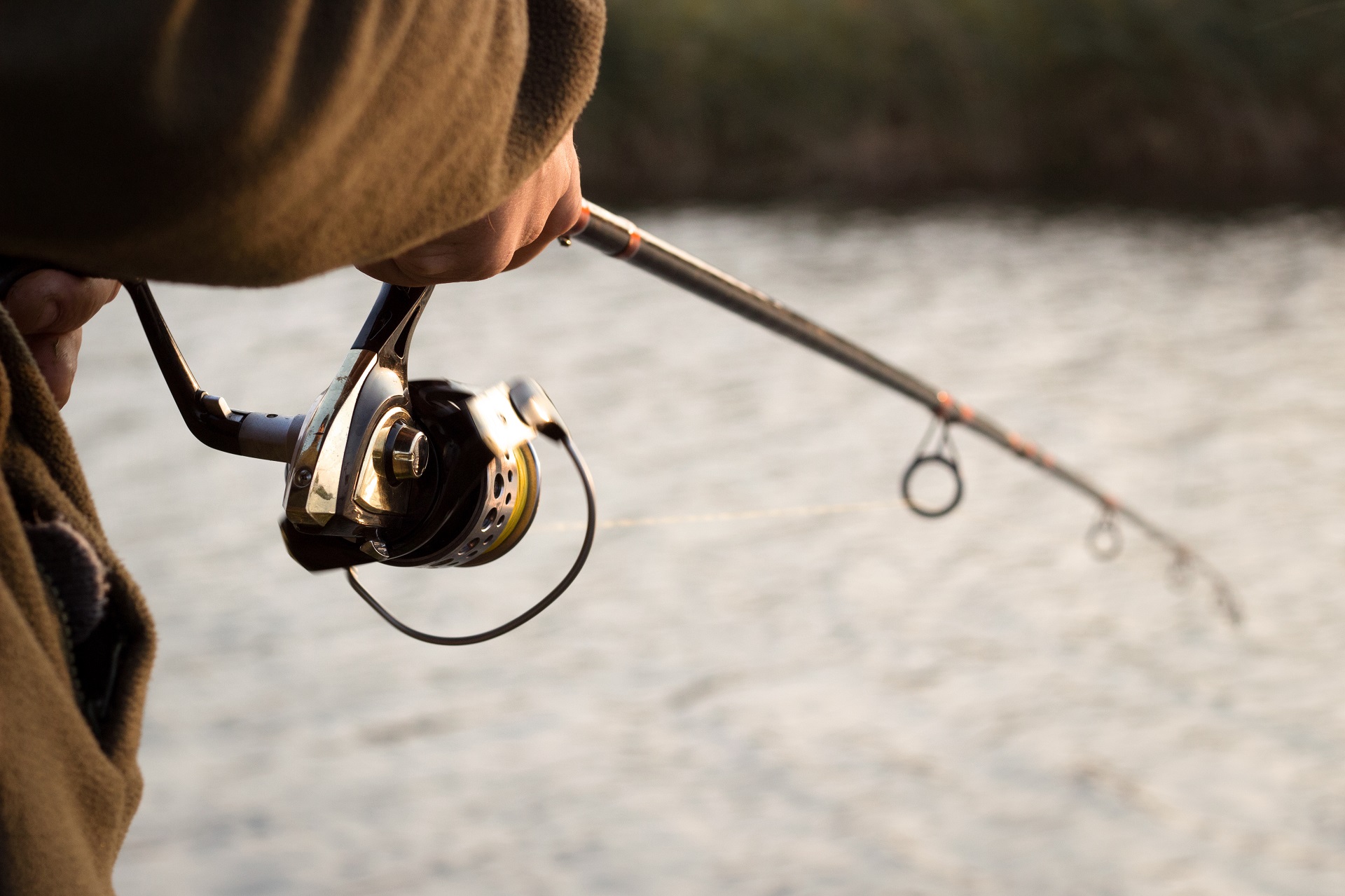 Nahaufnahme von einer Person mit einer Angelrute die an einem Fluss steht und fischt.