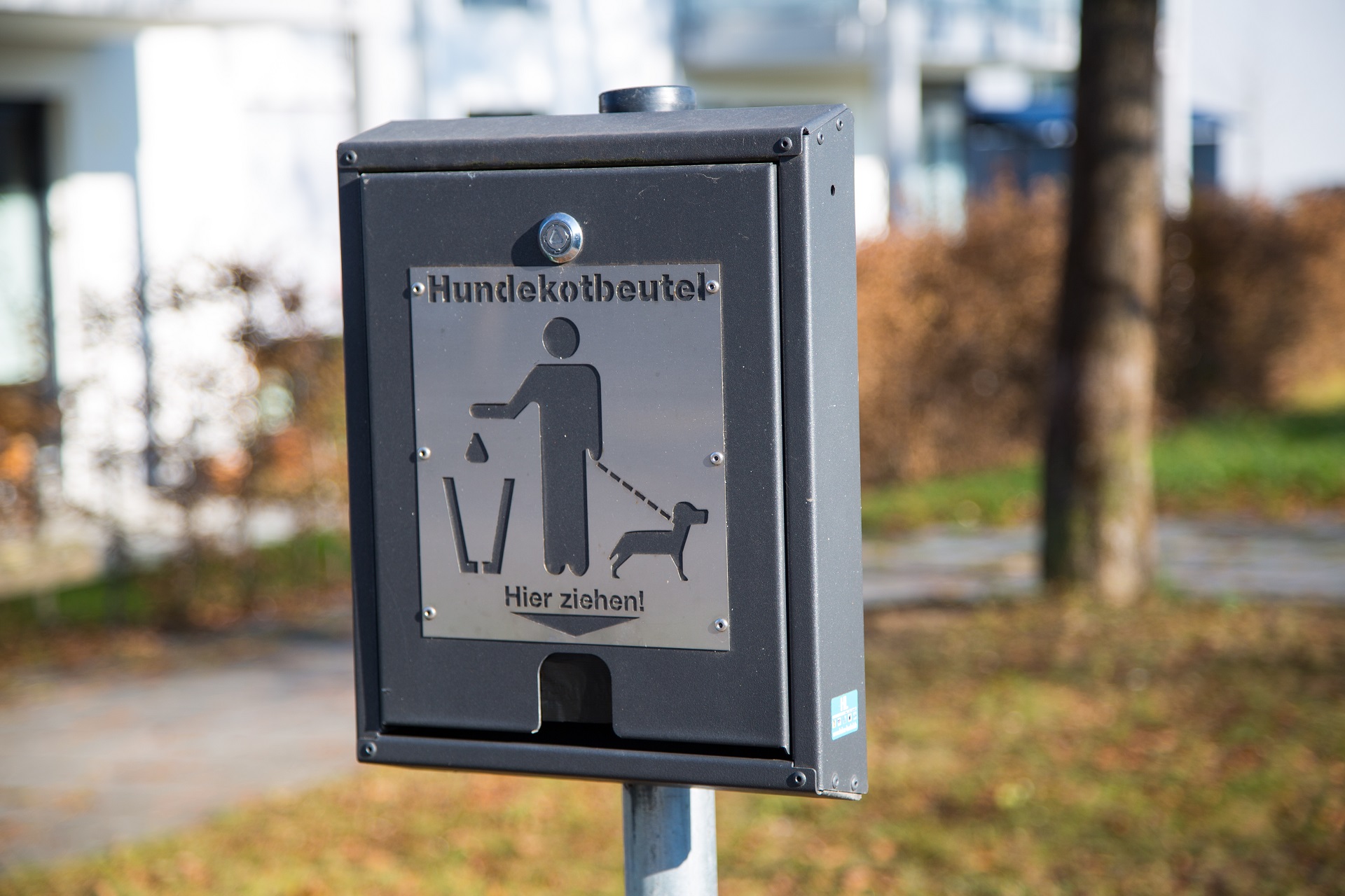 Eine Kotbeutelspender hängt in Wohnanlage und weist darauf hin, dass man die Hinterlassenschaften seines Hundes entfernt soll.