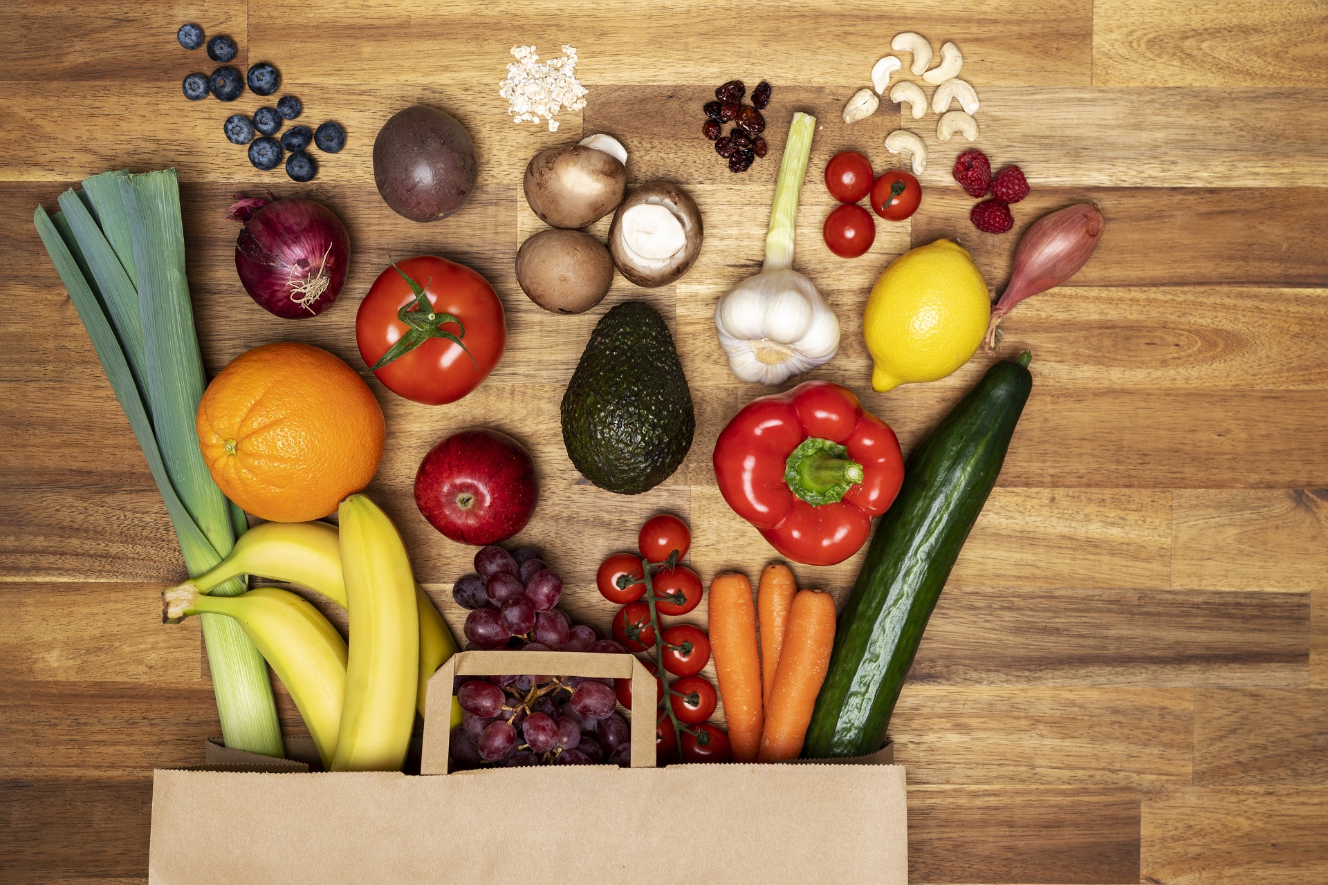 Eine Einkaufstasche voller gesundem Obst und Gemüse liegt ordentlich ausgebreitet auf dem Tisch.