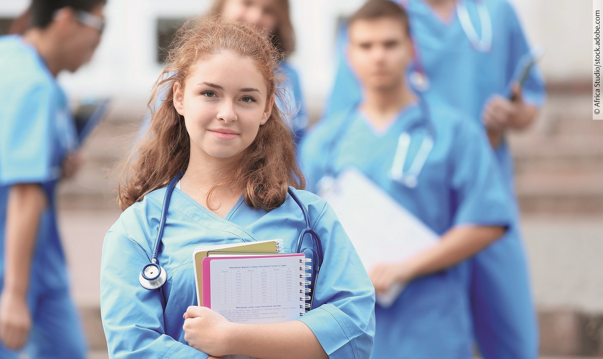 Eine Medizin-Studierende Person hält einen Block in den Armen und schaut in die Kamera.