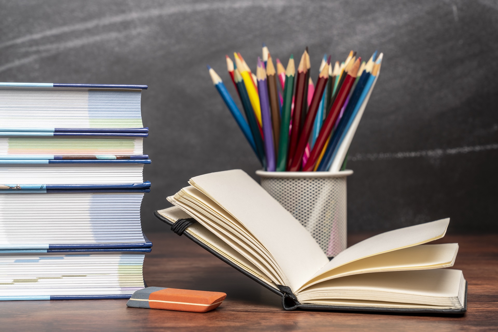 Ein aufgeschlagenes Buch liegt neben weiteren Büchern und Stiften auf einem Schreibtisch.