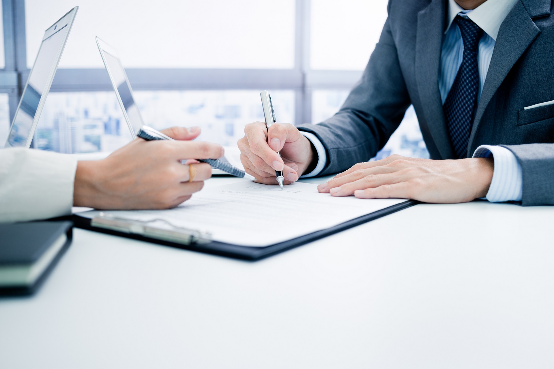 Zwei Personen sitzen sich gegenüber an einem Tisch. Zwischen ihnen liegen Dokumente..